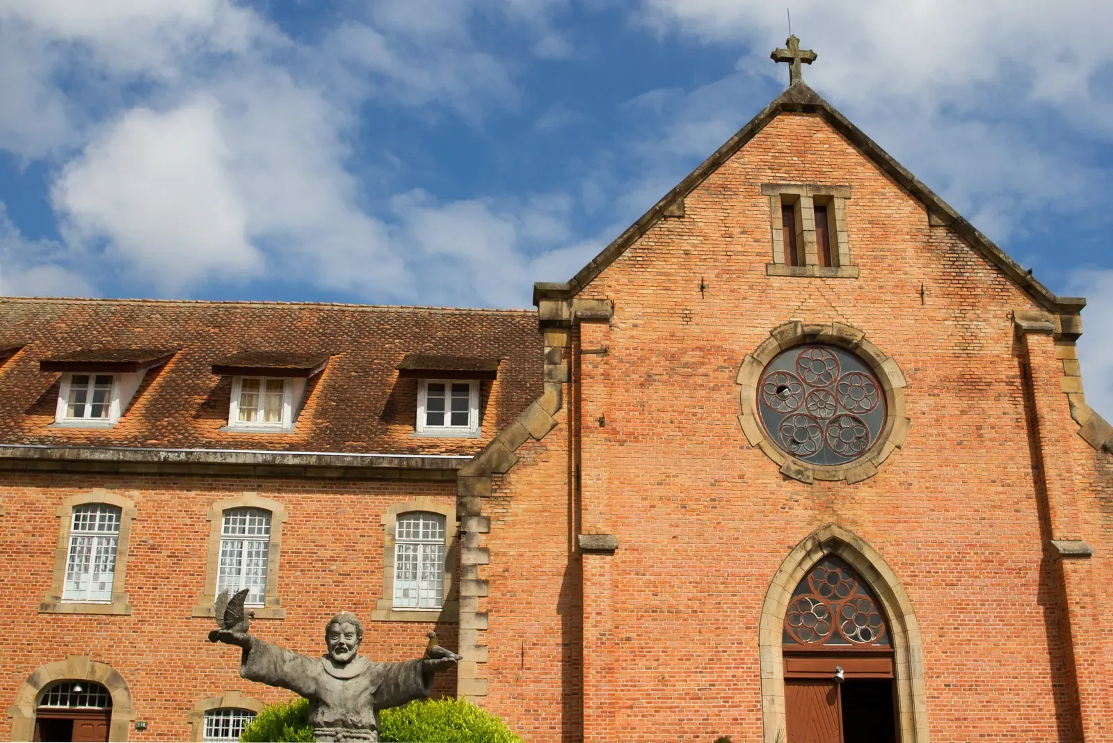 Fachada de tijolo aparente do Convento Franciscano de Lages, com rosácea e a estátua de um frade na frente