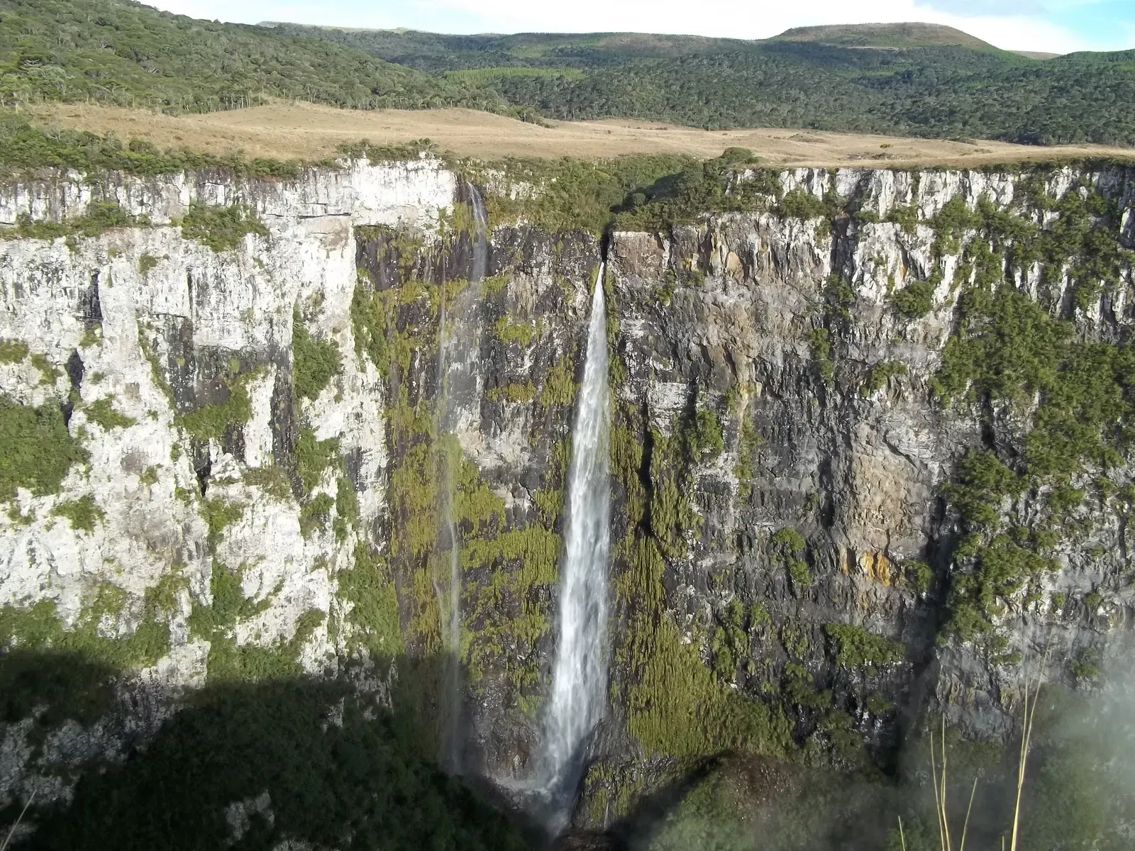 Cachoeira fina caindo por um paredão alto de basalto coberto de mata, no Cânion das Laranjeiras