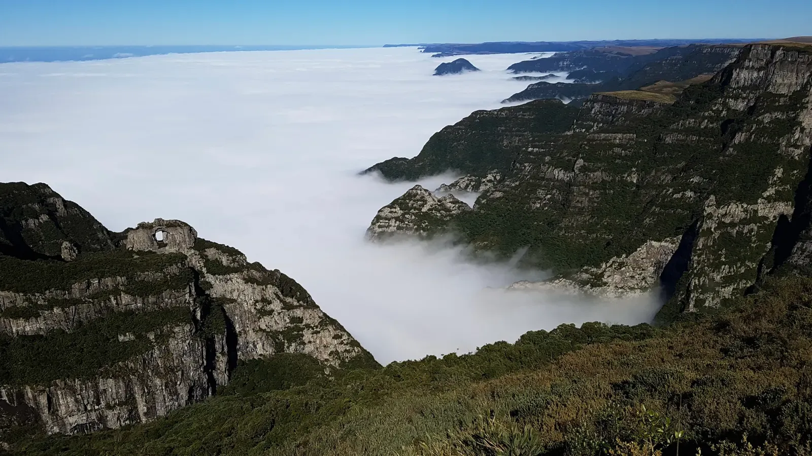 Paredões do Morro da Igreja, com a Pedra Furada à esquerda, acima de um mar de nuvens que cobre o vale